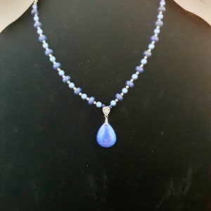 May include: A blue gemstone pendant necklace with a teardrop-shaped stone and a silver chain. The necklace is made with blue and silver beads.