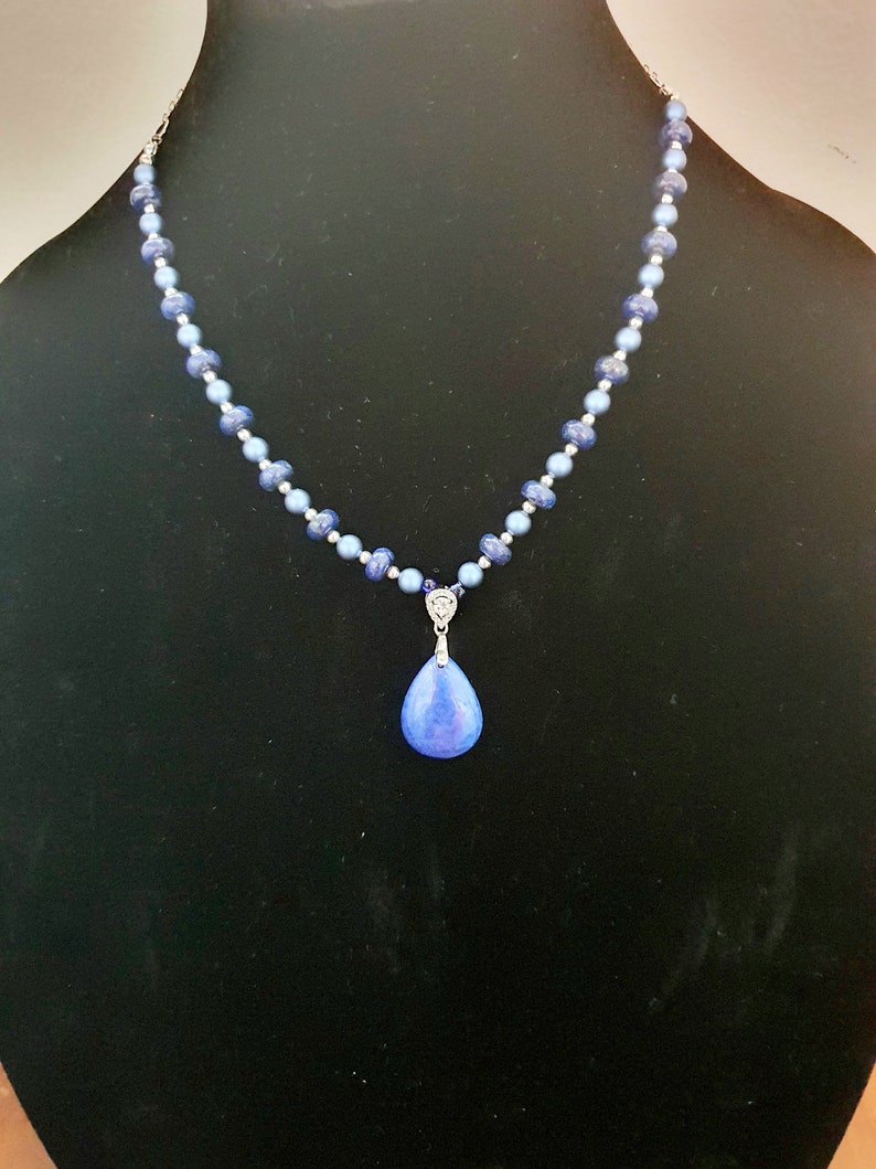 May include: A blue gemstone pendant necklace with a teardrop-shaped stone and a silver chain. The necklace is made with blue and silver beads.