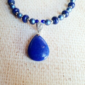 May include: A blue gemstone pendant necklace with a teardrop-shaped stone and a silver chain. The necklace is made of blue beads and silver beads.