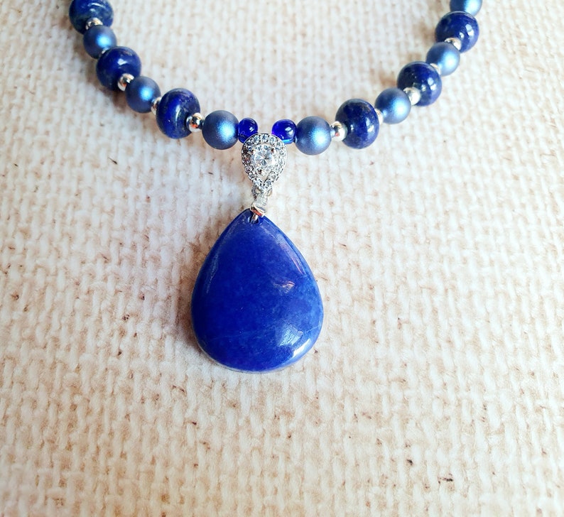 May include: A blue gemstone pendant necklace with a teardrop-shaped stone and a silver chain. The necklace is made of blue beads and silver beads.