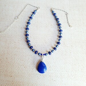 May include: A silver chain necklace with a teardrop-shaped blue pendant. The necklace is made of blue beads.