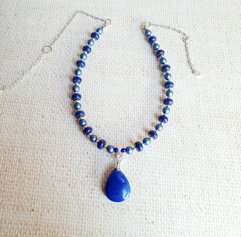 May include: A silver chain necklace with a teardrop-shaped blue pendant. The necklace is made of blue beads.
