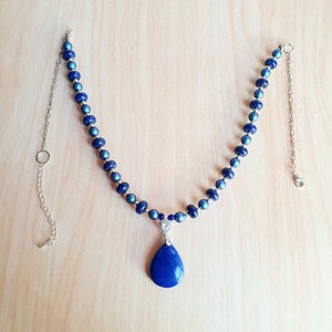 May include: A blue and silver necklace with a teardrop-shaped lapis lazuli pendant. The necklace is made of small, round beads and has a silver chain.