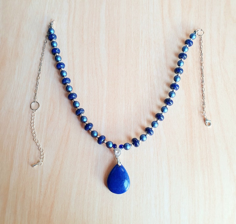 May include: A blue and silver necklace with a teardrop-shaped lapis lazuli pendant. The necklace is made of small, round beads and has a silver chain.