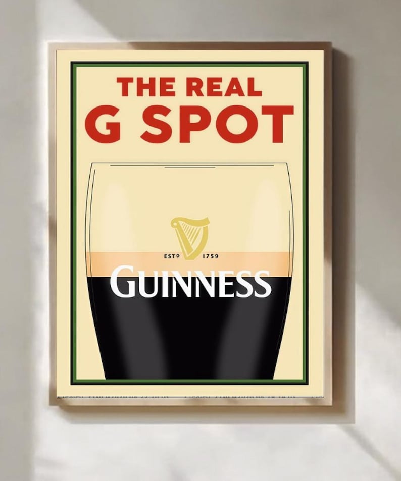 May include: Framed print of a Guinness pint, with the text "THE REAL G SPOT" in red. The Guinness logo and name are visible. The background is a light beige color, and the print is in a wooden frame.