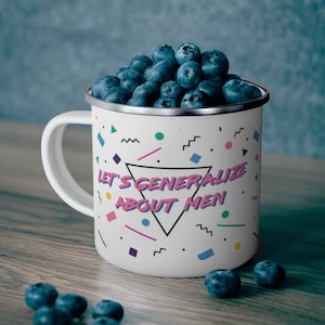 May include: White enamel mug with a colourful geometric pattern and the text "Let's generalize about men". The mug is filled with blueberries.