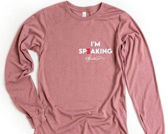 May include: A long-sleeved t-shirt in a dusty rose color with the text "I'M SPEAKING" in white with a red, white, and blue stripe design. The text is followed by a handwritten signature.
