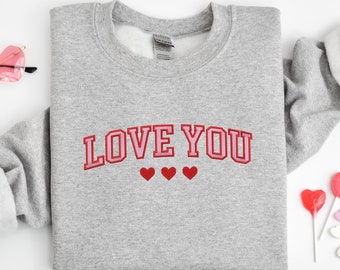 May include: A gray sweatshirt with the text "LOVE YOU" in pink and red letters with three red hearts underneath.