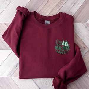 May include: Burgundy sweatshirt with a green graphic that says "I like them real thick and spruce" with two green stylized Christmas trees.