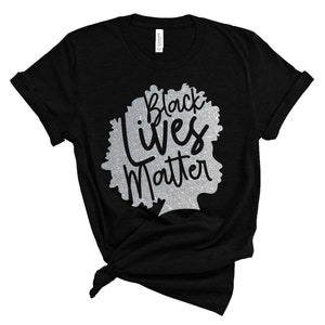 May include: Black t-shirt featuring a silver glitter design of a silhouette with the words "Black Lives Matter". The shirt is knotted at the bottom. The design is a statement of solidarity and support.