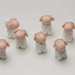 Puede incluir: Nueve figuritas de ovejas blancas con caras rosadas y ojos negros. Las ovejas están hechas de un material suave y texturizado y miden aproximadamente 5 cm de alto.