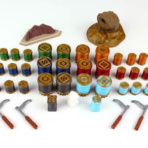 May include: A set of game pieces for a board game. The pieces include a variety of colors, including green, blue, red, orange, and gold. There are also two gray hooks, a white cube, and a gray cube. The pieces are arranged on a white surface.