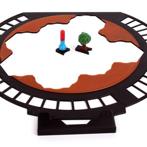 May include: A black circular game board with a brown terrain and a red and blue tower and a green tree on the board.