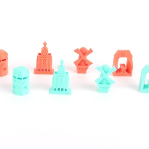 Op de afbeelding: Een set van acht miniatuur 3D-geprinte gebouwen in koraal- en turquoisekleuren. De gebouwen omvatten een windmolen, een kerk, een toren en een poort.