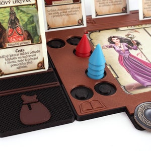 Pu&ograve; includere: Un gioco da tavolo con un tabellone di legno marrone, un pezzo da gioco rosso e blu, e una carta che dice "L&eacute;čiv&yacute; lektvar může&scaron; odhodit kdykoliv na uzdraven&iacute; 1 života, nebo k ochr&aacute;ně pomocn&iacute;ka před zabit&iacute;m."