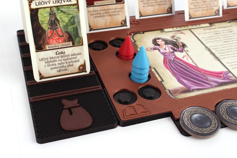 Pu&ograve; includere: Un gioco da tavolo con un tabellone di legno marrone, un pezzo da gioco rosso e blu, e una carta che dice "L&eacute;čiv&yacute; lektvar může&scaron; odhodit kdykoliv na uzdraven&iacute; 1 života, nebo k ochr&aacute;ně pomocn&iacute;ka před zabit&iacute;m."