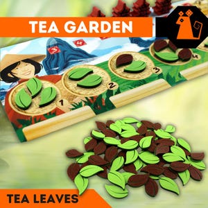 Könnte beinhalten: Ein Brettspiel namens "Tea Garden" mit grünen und braunen Teeblättern. Das Spielbrett zeigt eine Comicfigur einer Frau mit einem Korb voller Teeblätter und einen Berg im Hintergrund. Das Spielbrett hat vier Felder mit den Zahlen 1 bis 4. Die Teeblätter sind auf einer grünen Oberfläche verstreut.