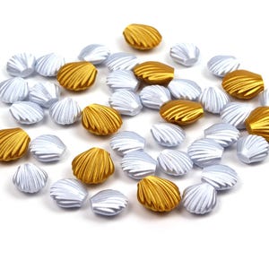 May include: A collection of gold and silver seashell-shaped beads. The beads are arranged in a random pattern on a white background.