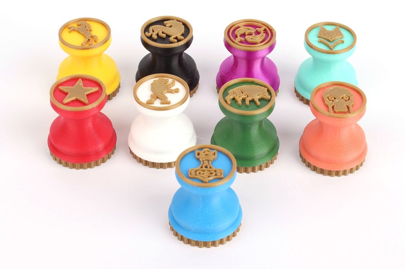 Op de afbeelding: Negen kleurrijke, ronde, dubbelzijdige stempels met een gouden rand. Elke stempel heeft een ander symbool, waaronder een ster, een paard, een leeuw, een wolf, een vis, een everzwijn, een schedel en een hamer.