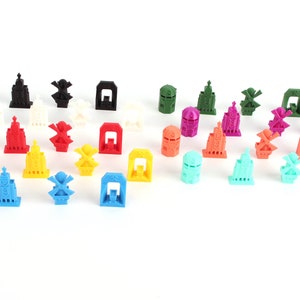 Op de afbeelding: Een verzameling kleurrijke 3D-geprinte miniatuurgebouwen en windmolens. De gebouwen zijn in verschillende kleuren, waaronder rood, blauw, groen, geel en paars. De windmolens zijn wit met zwarte bladen.