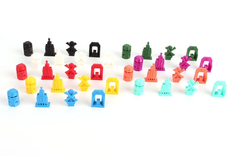 Op de afbeelding: Een verzameling kleurrijke 3D-geprinte miniatuurgebouwen en windmolens. De gebouwen zijn in verschillende kleuren, waaronder rood, blauw, groen, geel en paars. De windmolens zijn wit met zwarte bladen.