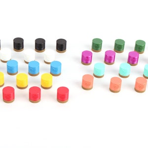 Op de afbeelding: Assortiment van kleurrijke plastic knoppen in verschillende kleuren, waaronder rood, geel, blauw, groen, wit, zwart, roze en oranje. De knoppen hebben een decoratief ontwerp en zijn in rijen op een wit oppervlak gerangschikt.
