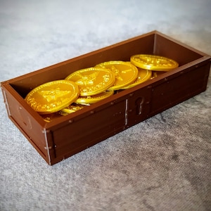 Pu&ograve; includere: Un forziere di legno marrone pieno di monete d'oro. Le monete hanno un disegno di un'ape.