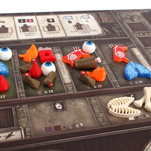May include: A board game with various coloured plastic pieces representing different body parts. The pieces are arranged in rows on the board, with labels in a foreign language. The board has a brown background with a medieval theme.