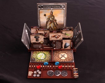 May include: A brown game board with a card holder and a character card that says "Strażnicze Prażdnooty". The board has a number track, a dice tray, and a token holder. There are also several cards in the card holder.