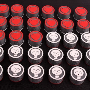 Puede incluir: Un conjunto de 36 piezas de juego, 18 son rojas con un diseño de corazón y 18 son blancas con un diseño de calavera. Las piezas son redondas y tienen una superficie texturizada.