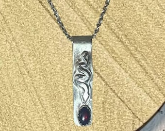 May include: A silver necklace with a pendant featuring a stylized snake design and a dark red gemstone.