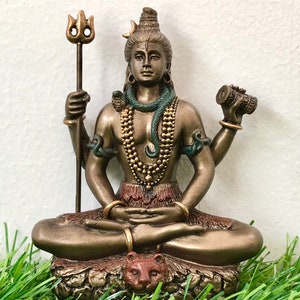 May include: A bronze statue of Shiva, a Hindu deity, sitting in a meditative pose. He is adorned with a snake, a necklace, and a third eye. He holds a trident in one hand and a drum in the other. The statue is sitting on a base with a tiger head.