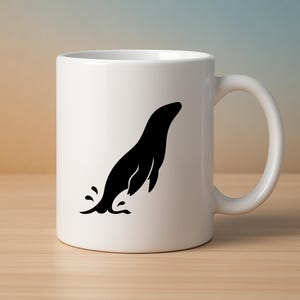 May include: White ceramic mug featuring a black silhouette of a seal leaping out of water. The mug has a curved handle and is set on a light brown wooden surface. The background has a gradient of beige, blue, and white.