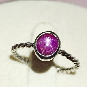 Peut inclure: Une bague en argent avec une bande torsadée et une pierre précieuse en rubis étoilé rose ronde.