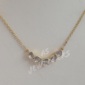 May include: A gold chain necklace with a row of six clear, faceted stones set in silver. The stones are arranged in a curved line.