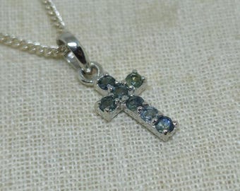 Puede incluir: Un collar de cadena de plata con un colgante de cruz de plata. La cruz está adornada con pequeñas piedras azules.