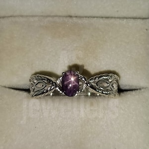 May include: A silver ring with a purple star-shaped gemstone set in a delicate, twisted band.