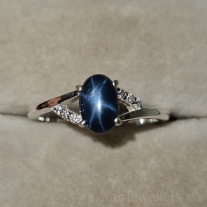 Könnte beinhalten: Ein silberner Ring mit einem blauen Stern-Saphir-Edelstein und kleinen weißen Diamanten, die in einem zarten Band gefasst sind.