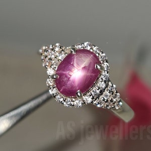 May include: A silver ring with a pink star ruby gemstone surrounded by smaller white gemstones.