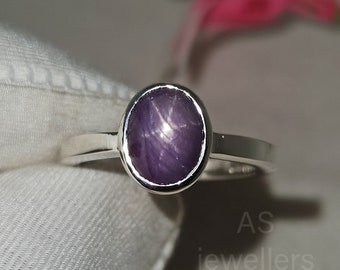 May include: A silver ring featuring a purple star sapphire gemstone. The ring has a plain band and the gemstone is oval in shape.