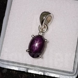 Op de afbeelding: Een zilveren hanger met een paarse ster-saffier edelsteen. De edelsteen is ovaalvormig en heeft een stervormig patroon.