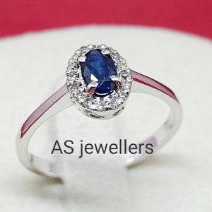 Peut inclure: Une bague en argent avec un saphir bleu ovale entouré d'un halo de petits diamants. La bague est sur un fond blanc avec le texte "AS jewellers" visible.