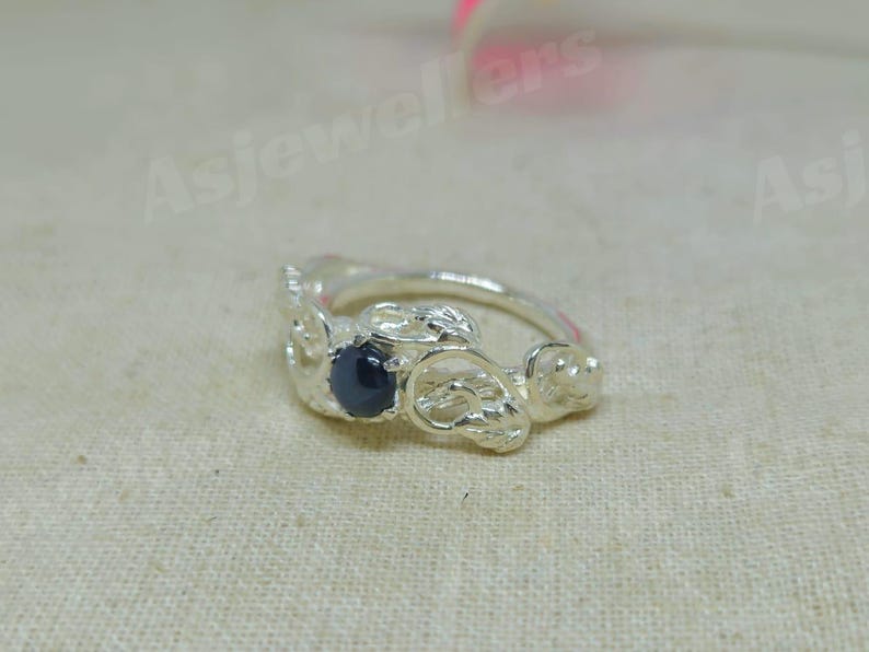 May include: A silver ring featuring a dark blue gemstone. The ring has an intricate, textured design with floral or organic shapes. The gemstone is round and centrally set.