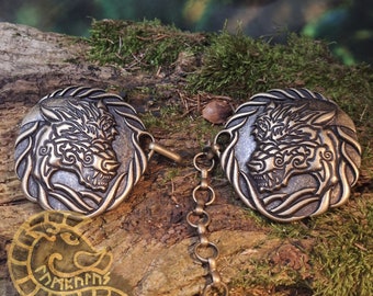 May include: Two bronze-colored metal clasps with a wolf design, connected by a chain. The clasps are round and have a detailed wolf head design with intricate patterns.