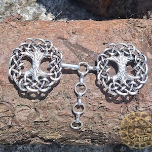 May include: A silver Celtic knotwork tree of life design with a chain connecting two circular pendants. The pendants are detailed with a tree of life design.