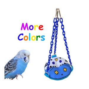 May include: A blue and white bird swing with a chain for hanging. The swing has a cartoon face with black eyes and a yellow beak. The swing is hanging from a white background. The text "More Colors" is written in rainbow colours above the swing.