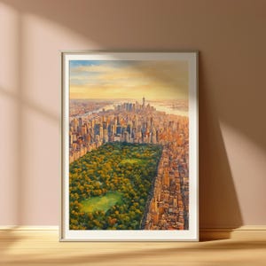 Op de afbeelding: Ingelijste aquarel schilderij van New York City vanuit vogelperspectief. Het kunstwerk toont Central Park omringd door wolkenkrabbers, met een warme, gouden-uur hemel. De schilderij wordt gepresenteerd in een witte lijst.