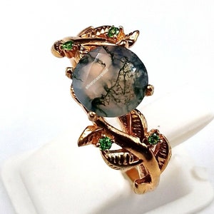 Peut inclure: Une bague en or avec une pierre précieuse en agate mousse et des accents verts. La bague présente un motif de feuilles.