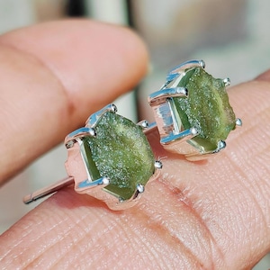 Op de afbeelding: Een paar zilveren oorbel studs met groene edelsteen bezettingen. De edelstenen zijn ruw geslepen en hebben een glinsterende, groene kleur.
