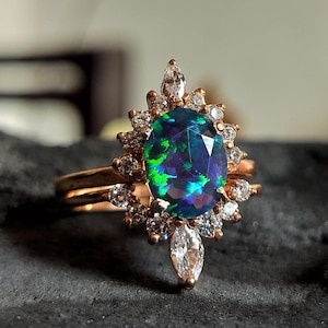 Op de afbeelding: Een ring van roségoud met een grote ovale opaal-edelsteen, omringd door een halo van kleinere diamanten. De ring zit op een delicate band.